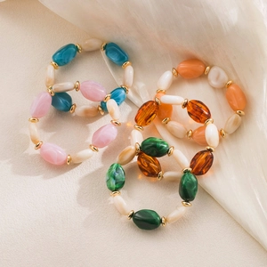Detalle de pulseras de cuentas de resina de colores con separadores dorados en fondo beige
