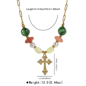 Close-up of golden hollow cross pendant with pearls and green beads on a dainty chain