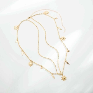 Detail of layered gold metal body chain featuring sun, moon and star charms on white background
