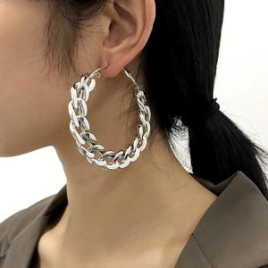 Close-up of large silver Cuban link hoop earrings worn by a model on white background
