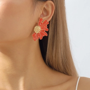 Close-up of a large red floral earring with gold trim worn by a model for fashion style