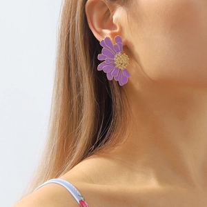 Detail view of purple daisy earrings with gold centers worn by a model on the ear