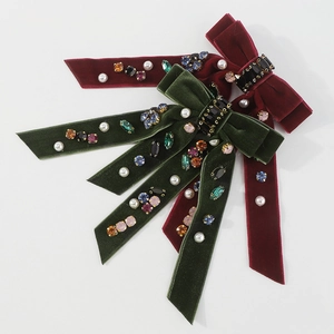 Close-up of velvet bow hair clips in burgundy and emerald green with pearl and crystal details