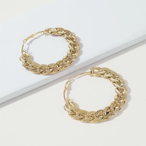 Detail shot of large golden chunky Cuban link chain hoop earrings on a white podium