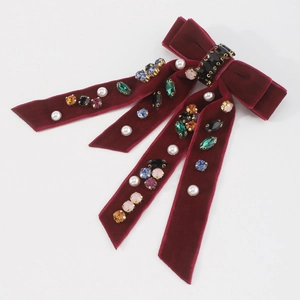 Macro view of burgundy velvet hair bow with colorful rhinestones and white pearls detail