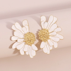 Close-up of elegant white enamel daisy earrings with gold trim on pink surface
