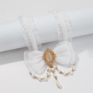 Macro detail of white lace ribbon with vintage golden opal pendant and dangling pearls
