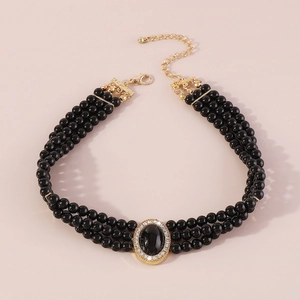Detailed view of triple-row black pearl necklace with vintage gold and crystal medallion