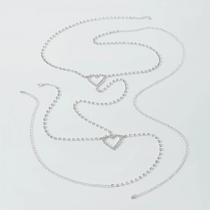 Détail de la chaîne de corps argentée avec pendentifs double cœur et strass brillants