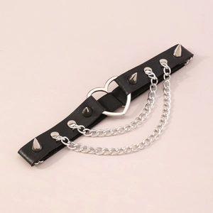 Dettaglio di un leg garter gotico in pelle nera con anello a cuore, catene e borchie