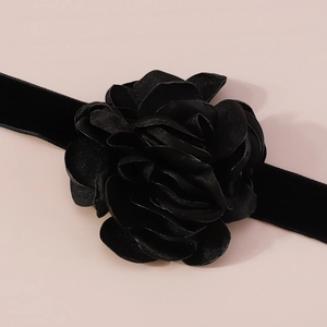 Détail d'une élégante rose en satin noir avec ruban en velours sur fond rose poudré