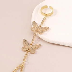 Close-up of gold butterfly hand chain ring with detailed embossing on cream background