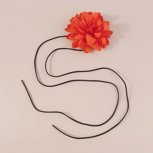 Gros plan d'un choker fleur en tissu orange avec cordon noir sur un fond rose tendre