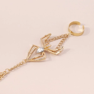Detailed view of golden spider hand chain bracelet with a teardrop crystal on a pink background