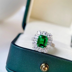 Emerald cut green crystal ring with halo diamond setting on a velvet jewelry box