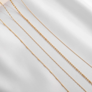 Selection of four 18K gold plated beaded chains displayed on white silk fabric background