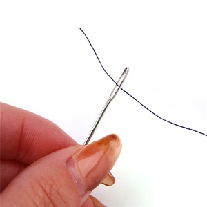 Detail of silver hand sewing needle with easy-thread design and blue thread