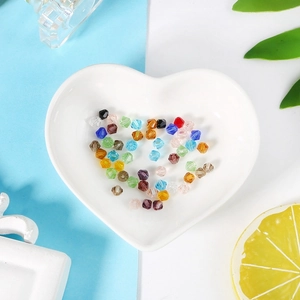 Colorful 4mm bicone faceted crystal beads scattered in a heart-shaped ceramic dish