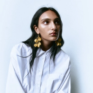 Detalle de pendientes de hoja dorada lucidos por una modelo con una camisa blanca