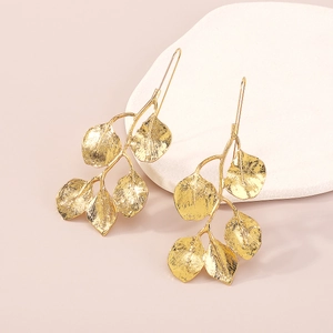 Pendientes largos de rama de hoja dorada con textura detallada sobre fondo rosa