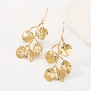 Detalle de pendientes de hoja dorados con textura martillada sobre piedra blanca
