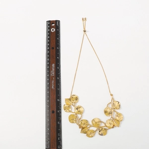 Detalle de un collar dorado con diseño de hojas junto a una regla de madera de escala