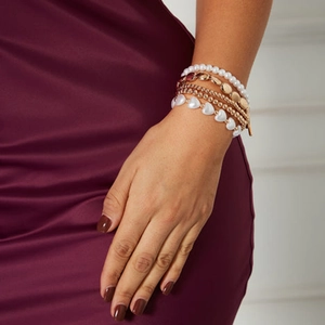 Detalle de set de pulseras de capas doradas con perlas y dije de corazón en la muñeca