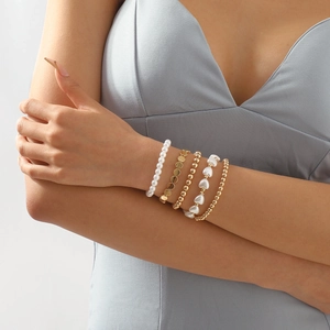 Detalle de un juego de 5 pulseras doradas de varias capas con perlas en la muñeca