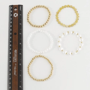 Detalle del juego de cinco pulseras elásticas de perlas y cuentas doradas con regla