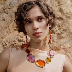 Close-up of geometric resin gemstone necklace and earrings on a model with rock background