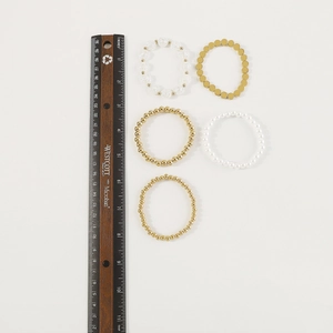 Vista detallada del juego de 5 pulseras multicapa con perlas y cuentas doradas con una regla