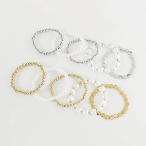 Detalle de set de 10 pulseras multicapa con cuentas doradas plateadas y perlas blancas