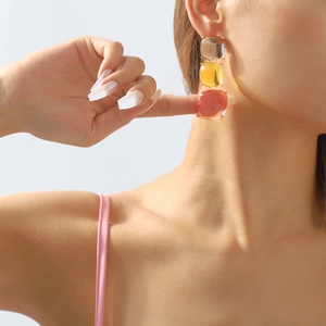Gros plan de boucles d'oreilles géométriques en résine grise, ambre et rose sur un modèle