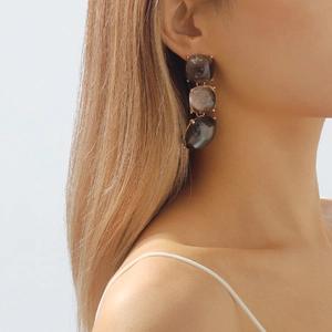 Détail de boucles d'oreilles bohèmes avec trois gemmes en résine gris fumé et plaqué or