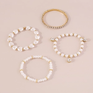 Detalle de un conjunto de 4 pulseras doradas y perlas con dijes de corazón y circón