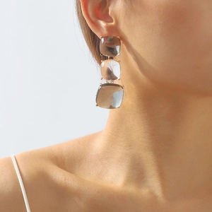 Détail de boucles d'oreilles géométriques à trois niveaux avec base dorée et pierres grises