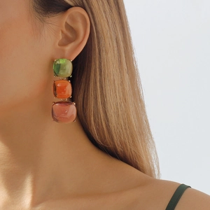 Gros plan de boucles d'oreilles géométriques en résine verte, orange et rouge sur un mannequin