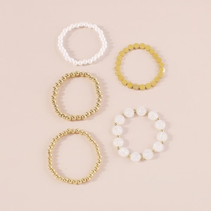 Detalle de un set de 5 pulseras de cuentas doradas y perlas con relieve de rosa blanca