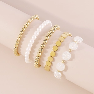 Detalle de un juego de 5 pulseras doradas y de perlas sobre un soporte rosa suave