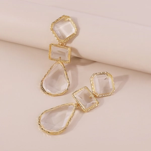 Macro detail of geometric drop earrings with gold metal frames and clear resin stones