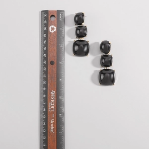 Détail de longues boucles d'oreilles noires avec griffes dorées et échelle de mesure