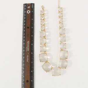 Détail d'un collier doré avec de grands cristaux de résine carrés et un fermoir mousqueton