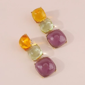 Détail de boucles d'oreilles géométriques en résine à trois niveaux orange, vert et violet