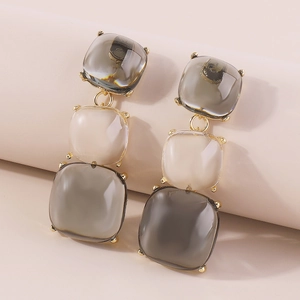Détail macro de boucles d'oreilles géométriques avec pierres en résine gris et blanc