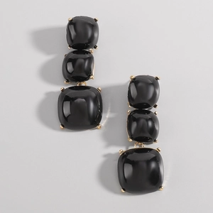 Détail de boucles d'oreilles triple carré noir avec griffes dorées sur gris