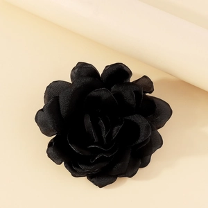 Detail of a black fabric rose brooch with elegant satin layers on a minimalist background
