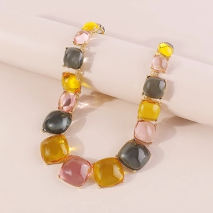 Détail d'un collier bohème en résine avec des maillons géométriques ambre, rose et gris