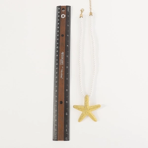 Primer plano del colgante de estrella de mar dorada con cuerda y regla para medir el tamaño
