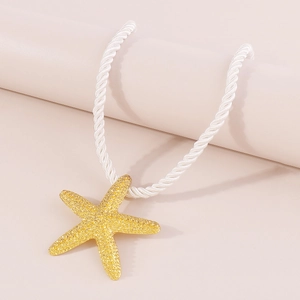 Detalle macro de un colgante de estrella de mar dorada sobre un cordón trenzado blanco