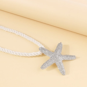Detalle de un colgante de estrella de mar plateado con pedrería y cordón blanco grueso
